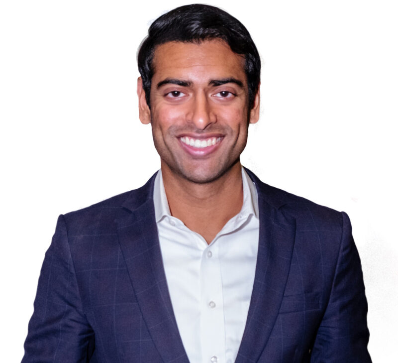 Man in a dark suit and white shirt smiling against a plain white background.